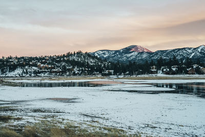 Scenic view of lake by snowcapped mountains against sky during sunset