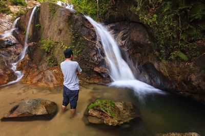 Rear view of woman standing on rock looking at waterfall