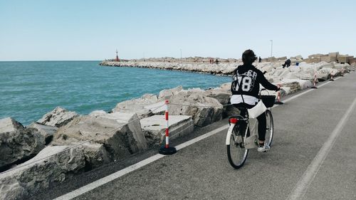 Rear view of woman cycling by sea on road