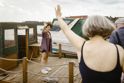 Happy young woman standing on houseboat waving at senior couple