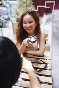 Portrait of a smiling young woman holding camera while sitting outdoors