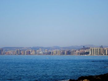 Sea by cityscape against clear blue sky