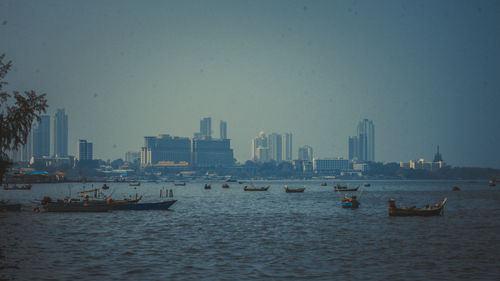 Boats in sea by buildings against clear sky