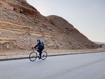 Man riding bicycle on road against mountain