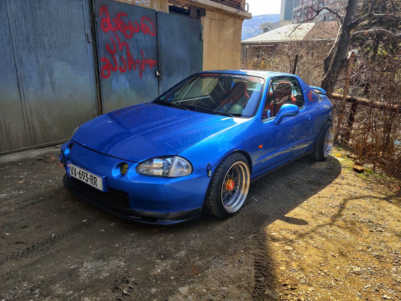 car, mode of transportation, vehicle, motor vehicle, transportation, land vehicle, architecture, blue, sports car, building exterior, retro styled, built structure, vintage car, wheel, city, day, old, automotive exterior, street, no people, bumper, graffiti, outdoors, automobile, abandoned, nature