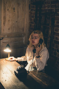 Young woman talking on rotary phone sitting in darkroom