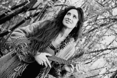 Tilt image of thoughtful woman holding ukulele at forest