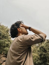 Side view of man covering his face against sky