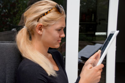 Side view of thoughtful beautiful young woman using digital tablet outside house