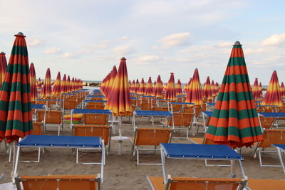 Empty chairs and tables at beach against sky