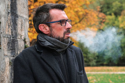 Mature man smoking cigarette standing against trees