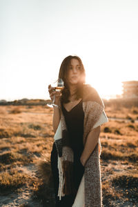 Young woman with a wine glass in a field at sunset