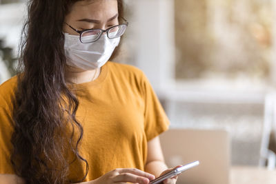 Young woman wearing mask using smart phone at home