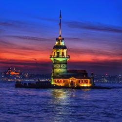 Illuminated tower by building against sky during sunset