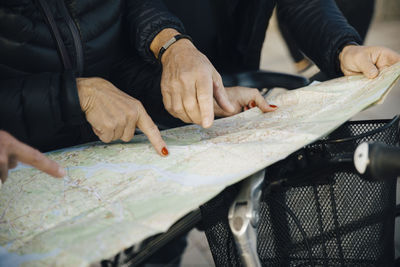 Midsection of senior friends with bicycle pointing at map during vacation