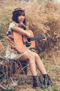 Portrait of young woman playing guitar on field