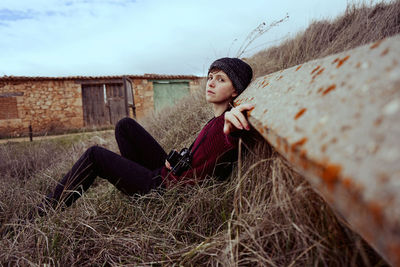 Portrait of young woman sitting on field against sky