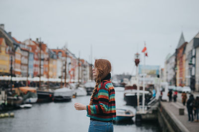 Side view of female standing against boats moored on shore of canal in copenhagen