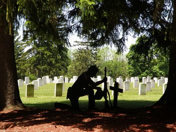 Silhouette veteran paying tribute by cross in cemetery