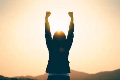 Silhouette woman with arms raised standing against sky during sunset