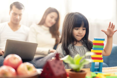 Girl playing with toy blocks by parents in living room at home