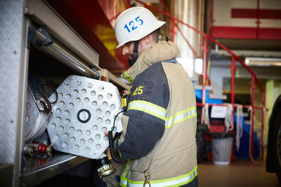 Side view of firefighter arranging fire hose in fire engine at station