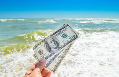 Cropped hand of man holding paper currency against sea