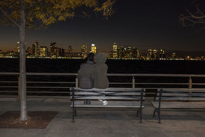 Two young women sitting on a park bench at the waterfront