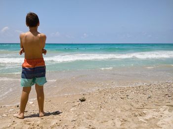 Shirtless boy standing at beach against sky