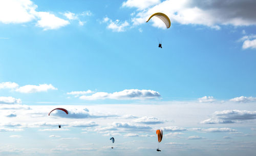 Low angle view of people paragliding against sky