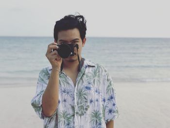 Portrait of man photographing while standing at beach