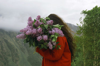 Woman holding flowers while standing on mountain