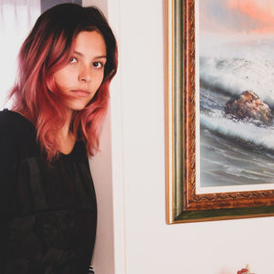 Portrait of young woman looking through window at home