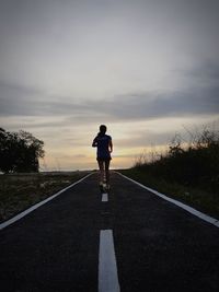 Rear view of lady on road against sky during sunset