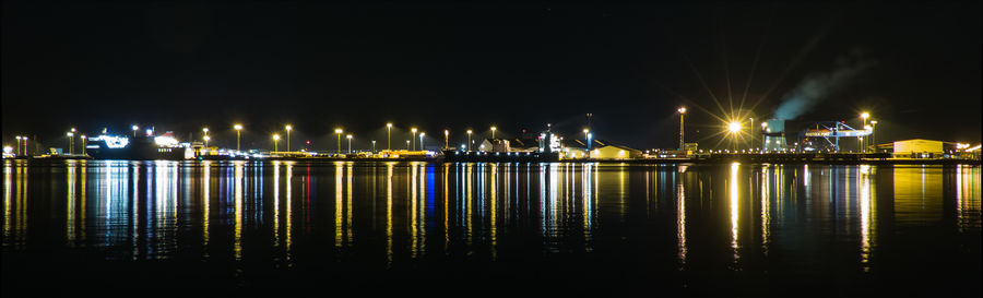 Illuminated lights by river against sky at night
