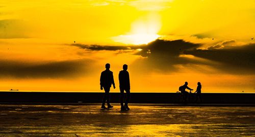 Silhouette people on beach against orange sky