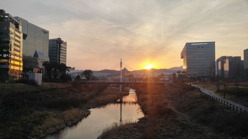 River amidst buildings in city against sky during sunset