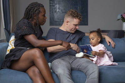 Multiracial family sitting with their daughter on a couch