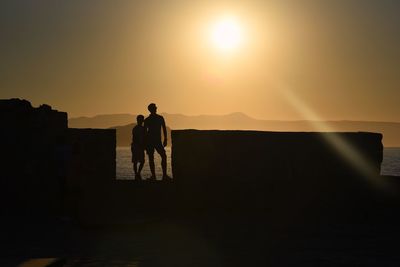 Silhouette men standing on landscape against sky during sunset