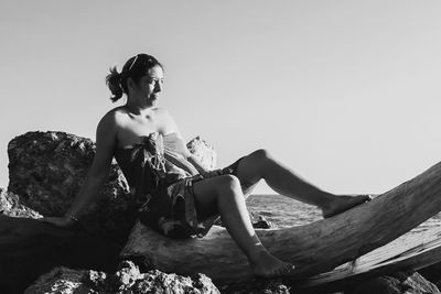 Young woman sitting on rock against sky