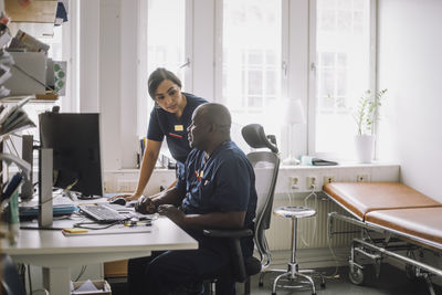 Female nurse discussing with male colleague sitting on chair at hospital