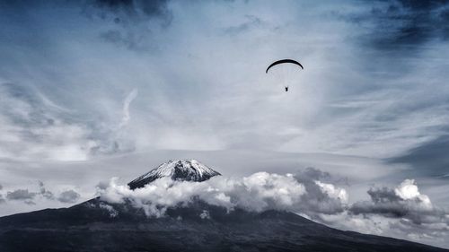 Low angle view of person paragliding over mountain against cloudy sky