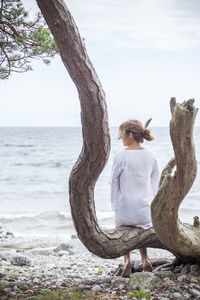 Woman sitting on tree on beach