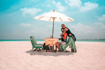 Man sitting on chair at beach against sky