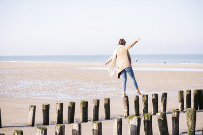 Rear view of person on wooden post at beach against sky