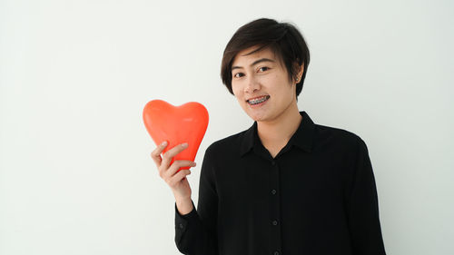 Portrait of smiling man holding heart shape against white background