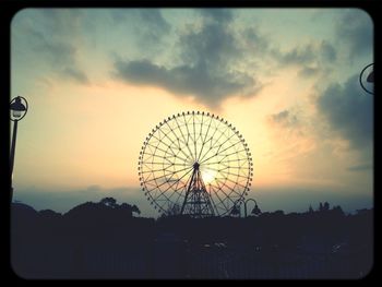 Low angle view of ferris wheel against cloudy sky