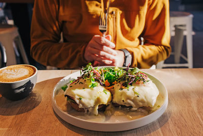 Unrecognizable man going to eat the brunch. eggs benedict on the plate , morning light