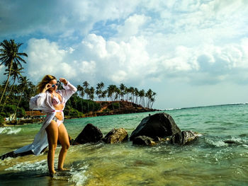 Young woman standing on rock by sea against sky