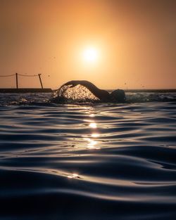 Person swimming in sea against sky during sunset